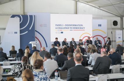 Conference room, filled with participants and people on stage in a panel debate 